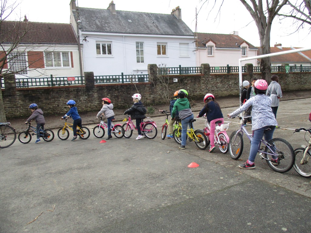 Dans une cour d'école, des enfants sont à l'arrêt sur des vélos en file indienne